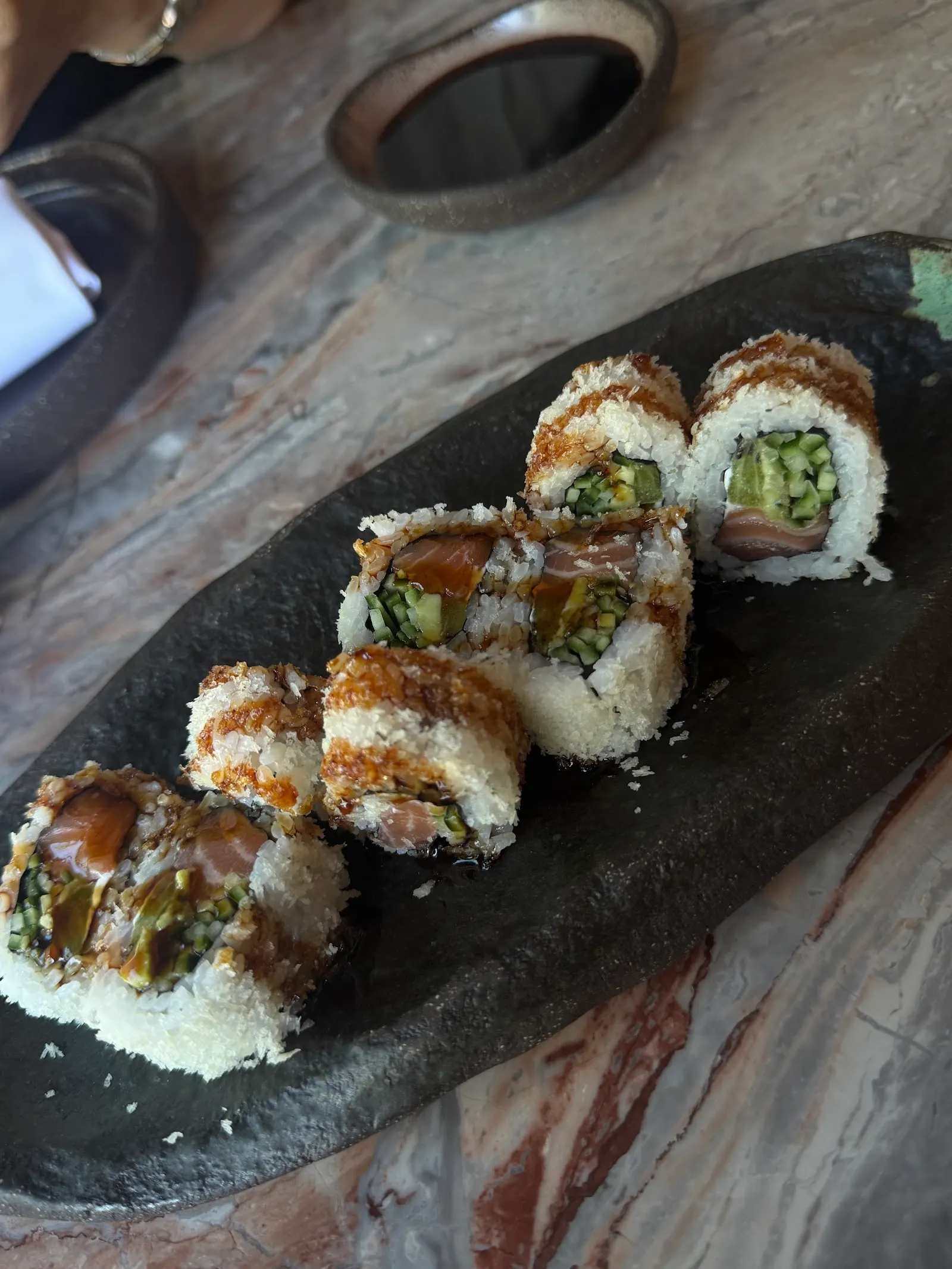 Sushi roll pieces arranged on a black slate plate on a wooden table.